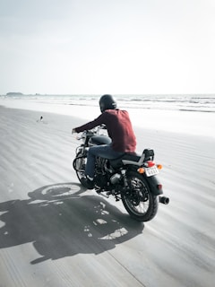 A rider wearing a helmet cruising along a coastal road with ocean waves in the background.
