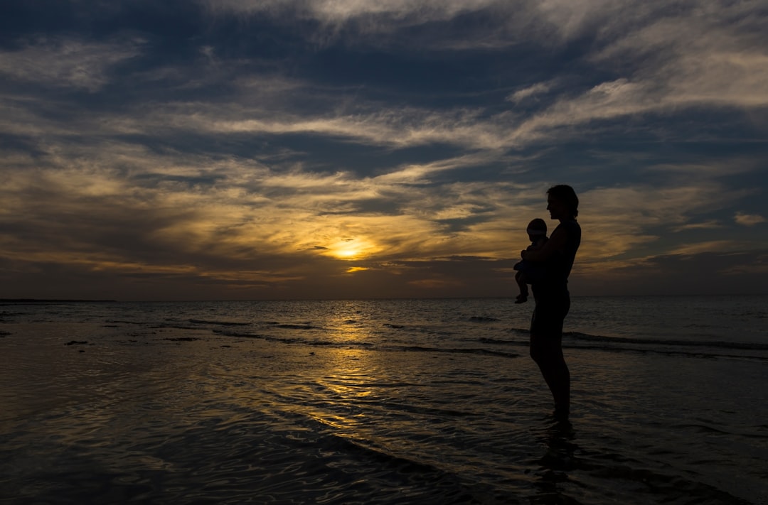 woman carrying baby on seashore during sunset