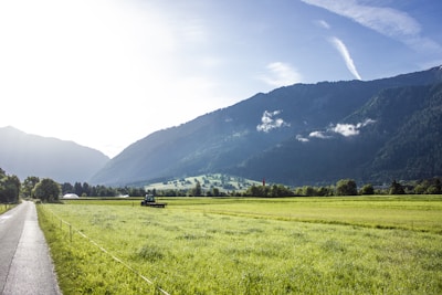 A green tractor plowing a field with mountains in the background.