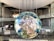 A large, spherical installation resembling a digital globe is suspended in a spacious, industrial-style indoor setting. The globe displays the Earth's continents and oceans, composed of pixelated panels. Metal structures, walkways, and glass railings surround the globe, with several people visible in the background.