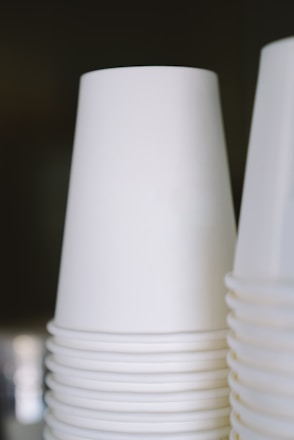 A clean, industrial photo of stacked paper cups and aluminum containers on a white background.