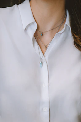 Layered necklaces with geometric pendants styled over a crisp white shirt.