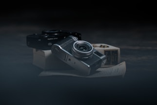 A moody dark-themed photo of a camera resting on a wooden table, surrounded by travel and wildlife prints.