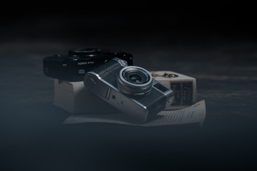 A moody dark-themed photo of a camera resting on a wooden table, surrounded by travel and wildlife prints.