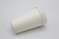 A plain, white disposable paper cup with a lid is positioned on its side against a neutral background. The cup appears to be clean and unused, suggesting it is for takeaway beverages.