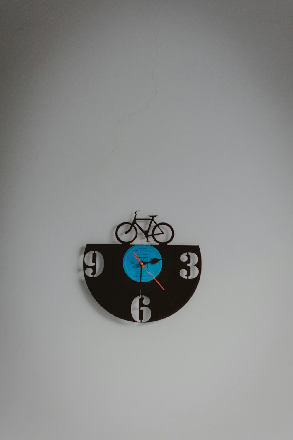 relógio de parede analógico preto e azul com tema de bicicleta exibindo o tempo de 3:30