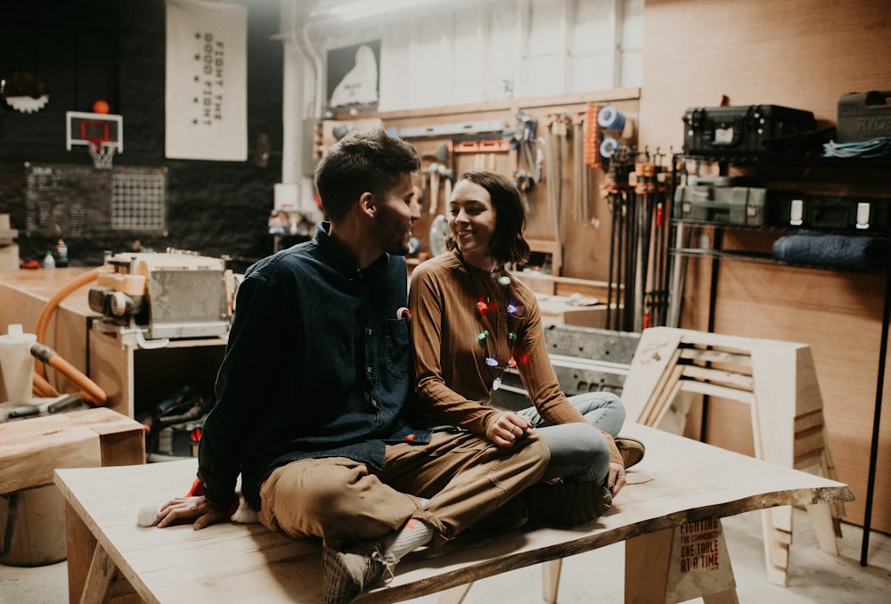 man and woman smiling and facing each other while sitting on table indoors