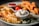 A plate featuring crinkle-cut fries, breaded and fried chicken strips, a small bowl of creamy sauce, and fresh cherry tomatoes. Garnishes include greens such as arugula, adding a touch of color and freshness.