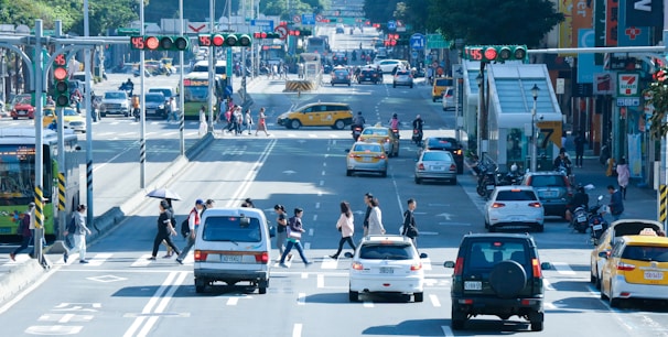 A busy city intersection with people crossing and vehicles waiting at traffic lights.