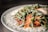 A close-up view of a plated dish featuring a vibrant red sauce topped with fresh green arugula, garnished with grated cheese. The background is softly focused, emphasizing the textures and colors of the ingredients.