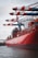A large red container ship named HAMBURG SÜD is docked at a port with multiple cranes transferring containers. The ship is loaded with multicolored shipping containers stacked high, and the sky is overcast.