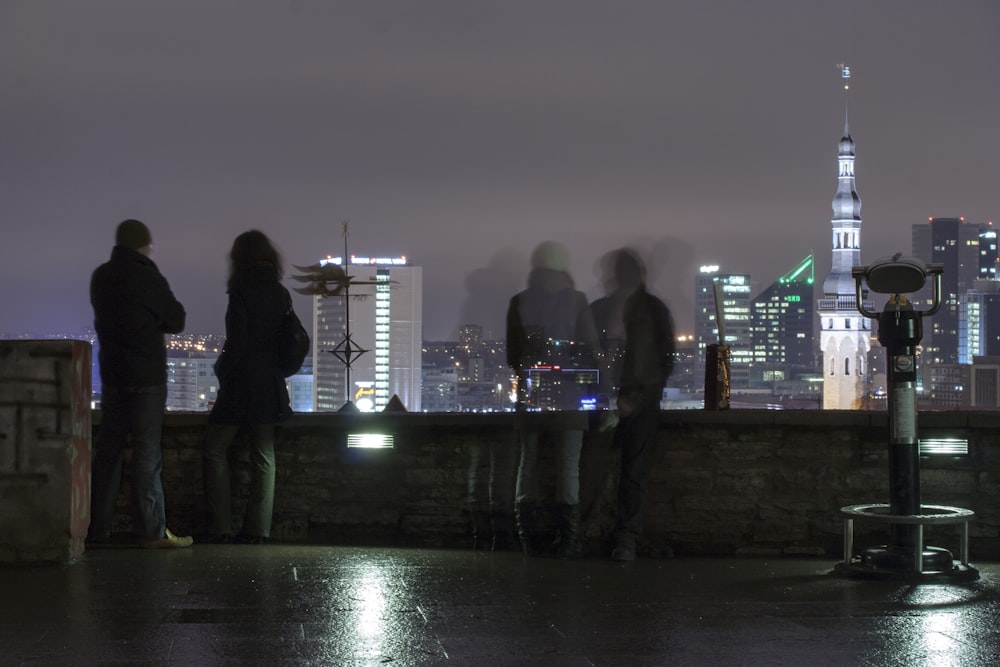 Cuatro personas de pie cerca de las barandillas que ven la ciudad con edificios de gran altura durante la noche