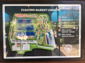 A detailed map of Floating Market Lembang is displayed, highlighting various attractions and facilities. There are icons indicating locations such as toilets, dining areas, a prayer room, beverage exchange points, and entrance points to the Rainbow Garden and the floating market itself.