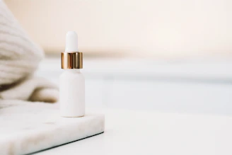 Close-up of a sleek Herzner serum bottle resting on soft ivory fabric with champagne gold accents.