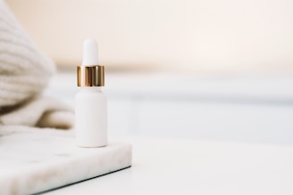 Close-up of a sleek serum bottle with a dropper, resting on smooth white marble.