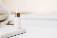 Close-up of elegant serum bottles with soft gold and blush accents on a white marble surface.