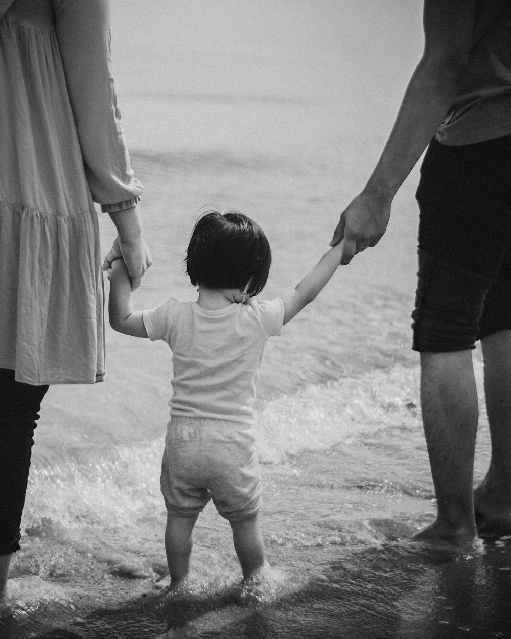 grayscale photography of two person holding hands of child while standing
