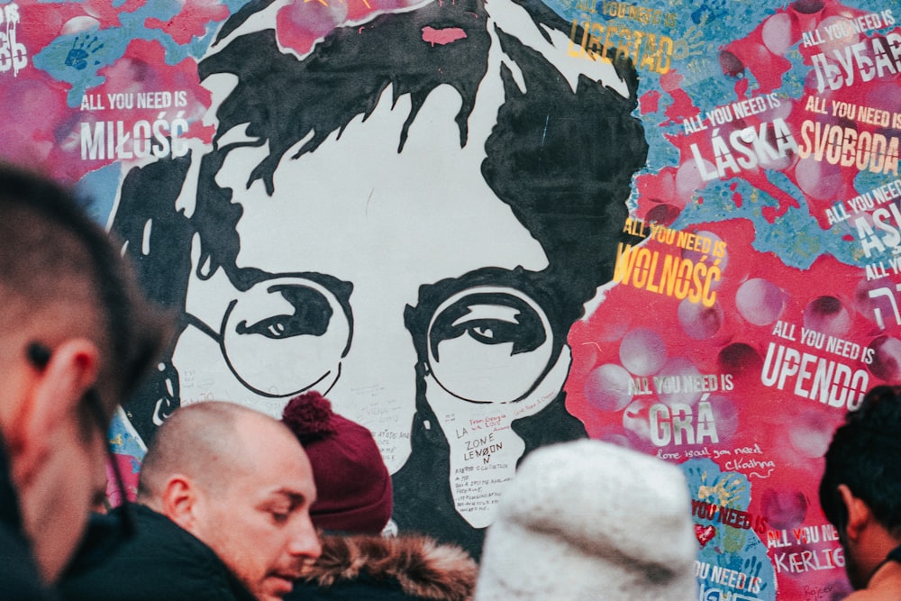 people near wall with graffiti art of John Lennon