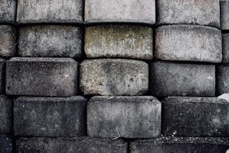 A wall constructed from large, rough-hewn stone blocks stacked in a uniform pattern. The blocks display a variety of gray tones, with some showing patches of moss and discoloration.