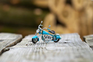 Motorcycle battery resting on a rustic wooden surface with a blurred road in the background.
