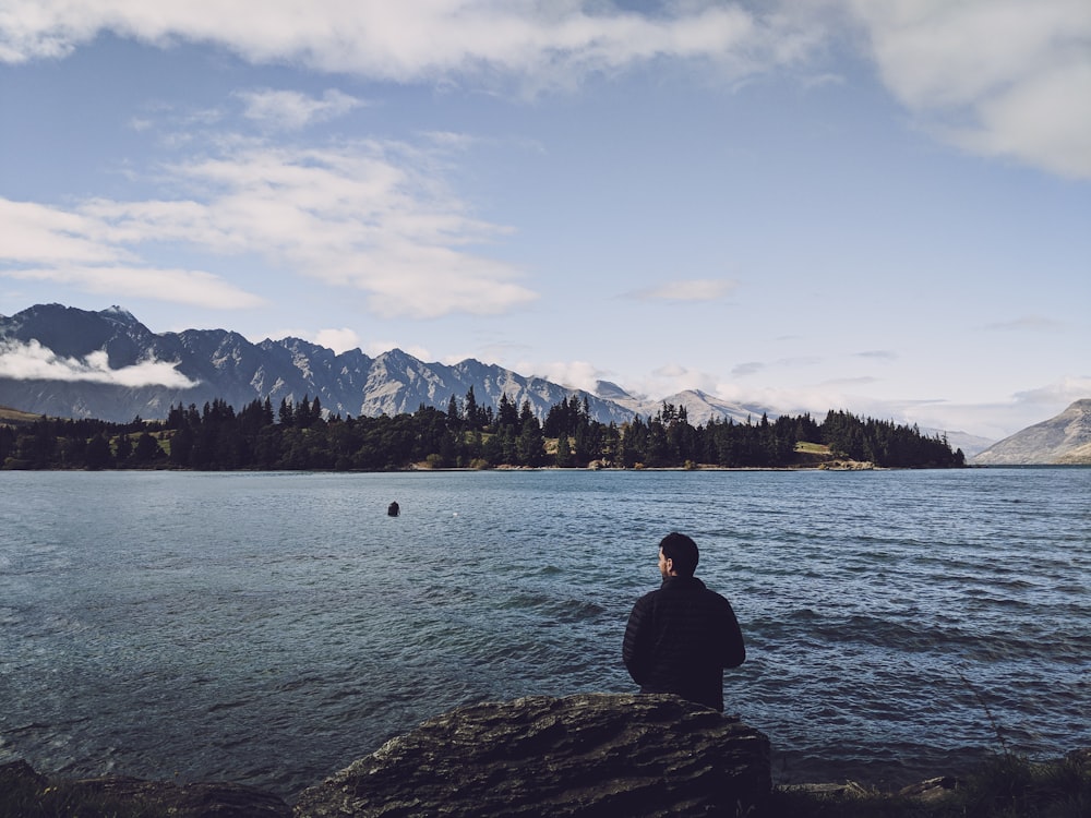 man sitting on rock in front of sea