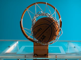 An action shot of a basketball swishing through a hoop with a clear blue sky background.