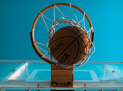 An action shot of a basketball swishing through a hoop with a clear blue sky background.