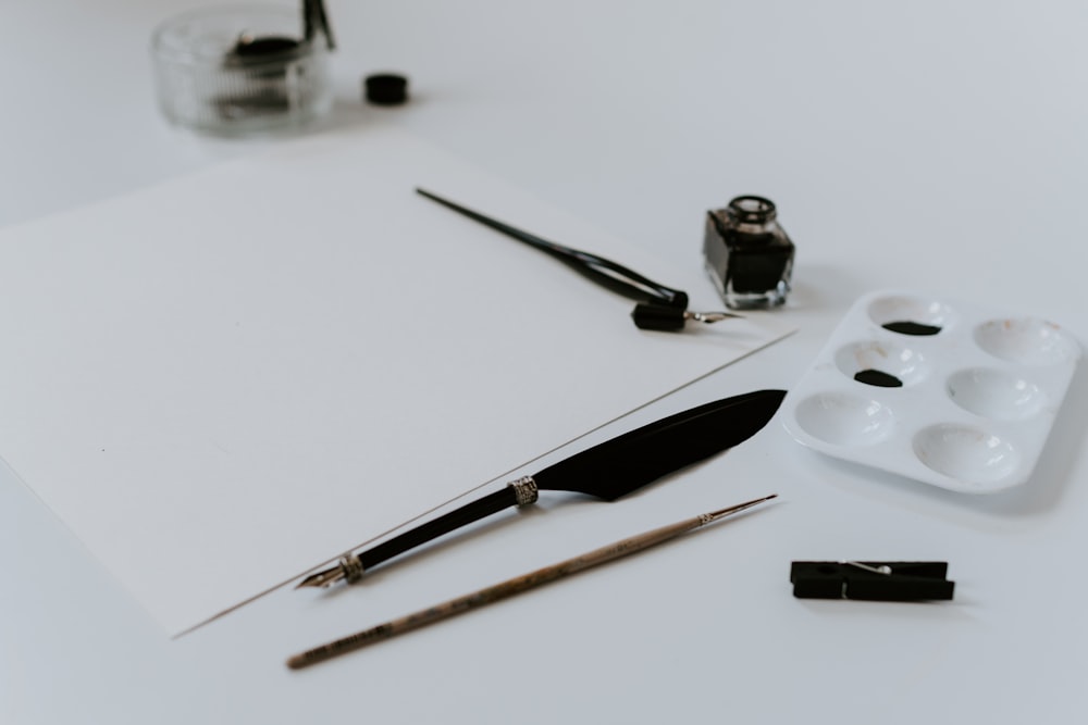 white paint palette with black paint beside ink bottle and paint brush