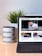 A tablet displaying a magazine website is positioned on a table, next to a mug with the word 'Bantumen' printed multiple times and a small potted plant. The tablet shows various articles and images on the screen.