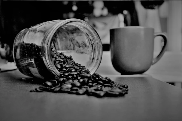 grayscale photography of coffee beans beside mug