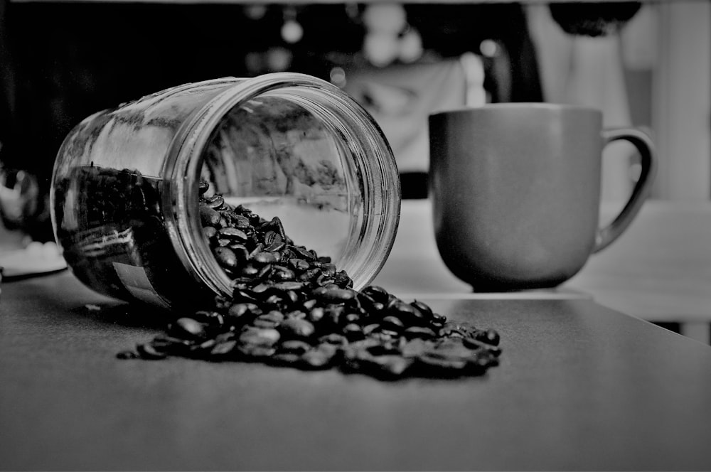 grayscale photography of coffee beans beside mug