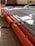 Several corrugated cables in orange and gray are neatly bound together with a black strap, lying on a wooden or concrete surface with sunlight casting shadows across them.