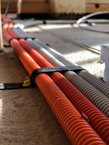 Several corrugated cables in orange and gray are neatly bound together with a black strap, lying on a wooden or concrete surface with sunlight casting shadows across them.
