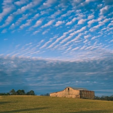 A sturdy timber frame barndominium nestled in a scenic rural landscape under a bright blue sky.
