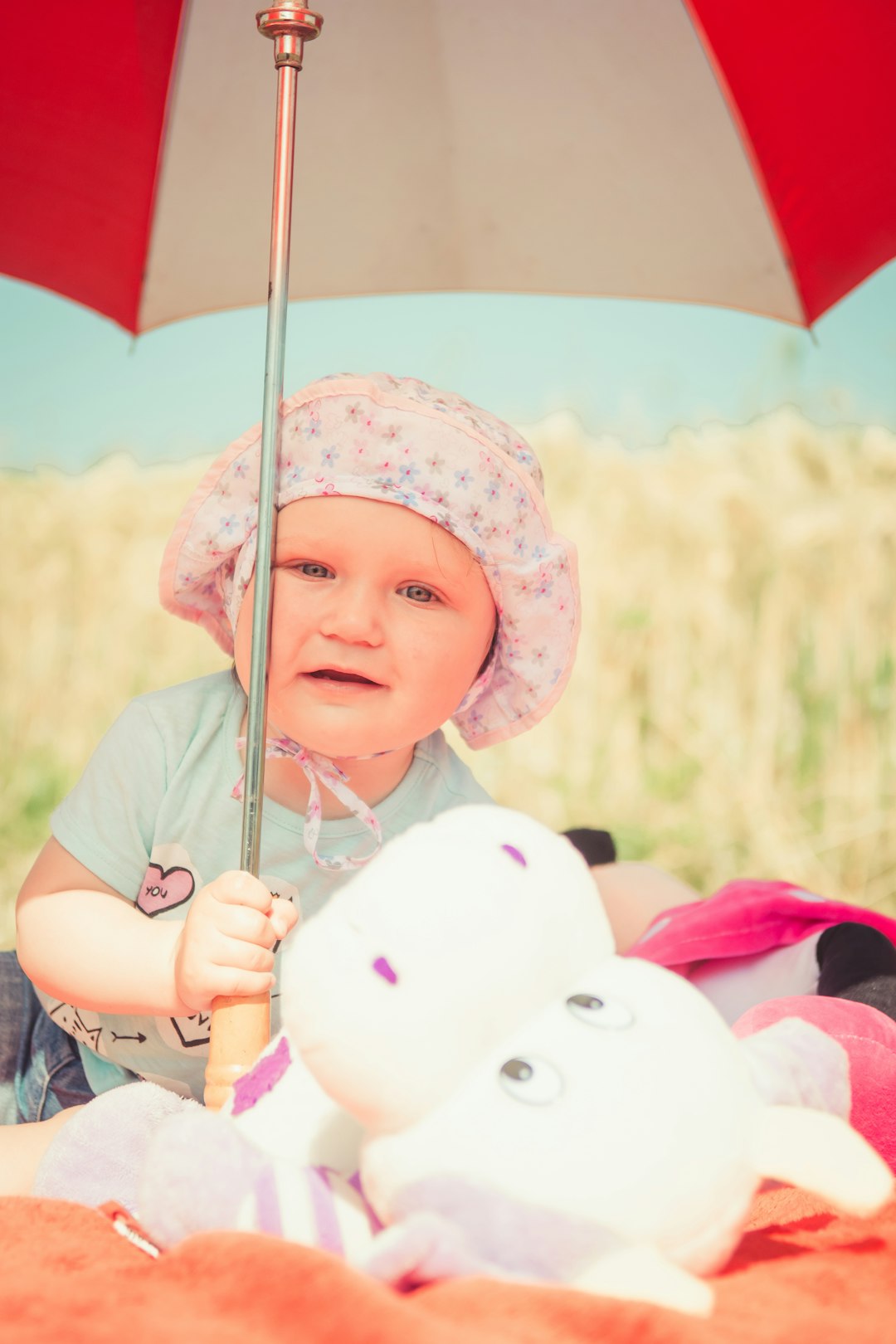 baby holding umbrella near plush toy