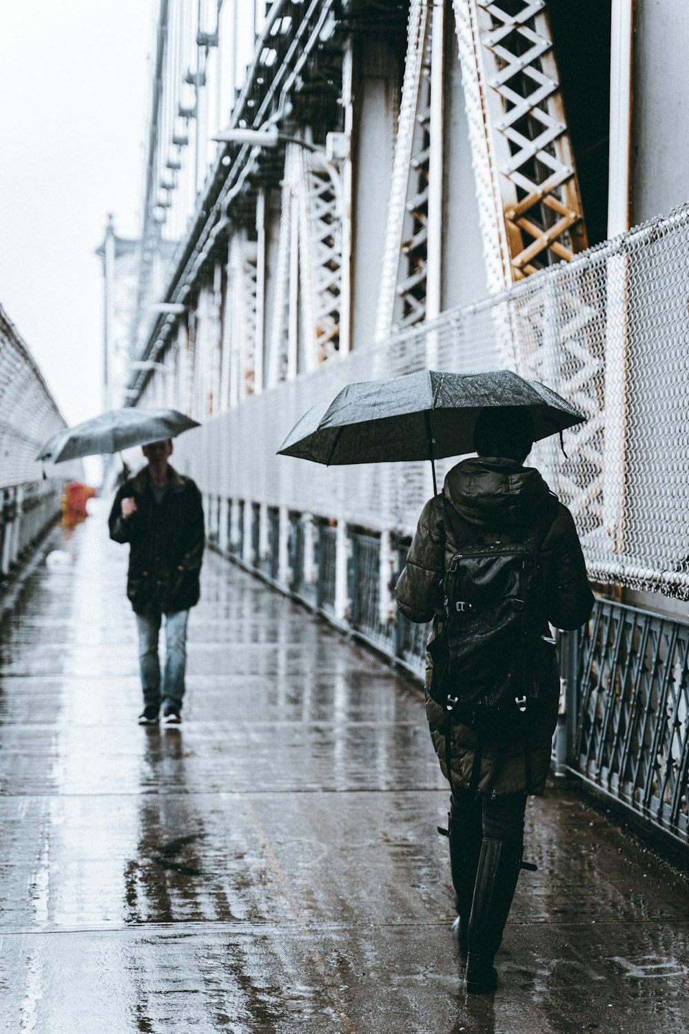 man and woman holding umbrellas walking in bridge