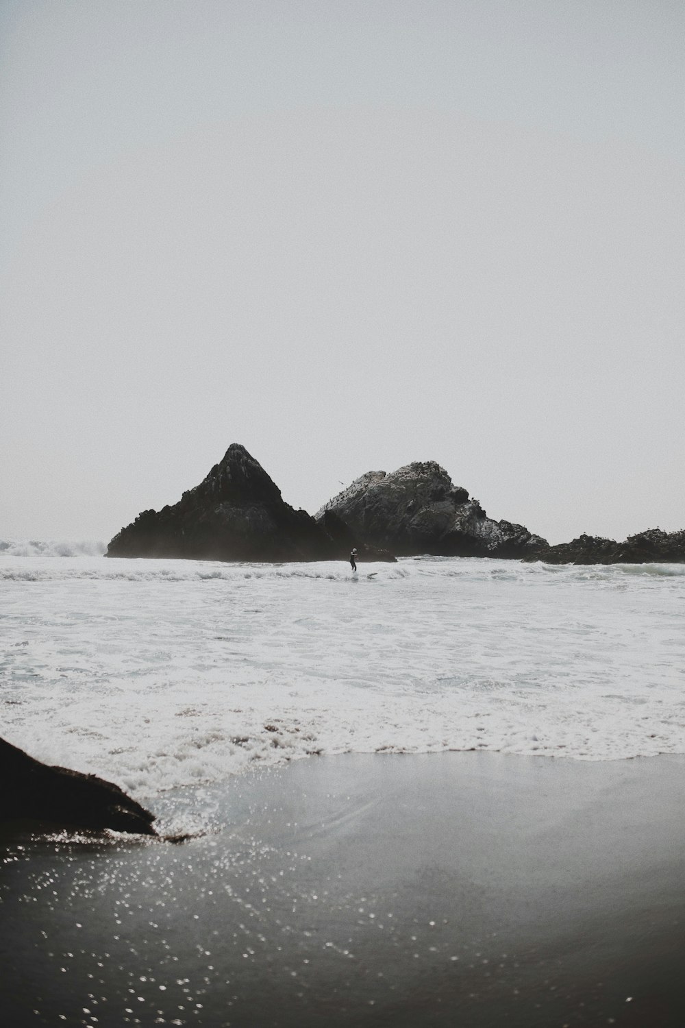 岩の近くのビーチでサーフィンをする人