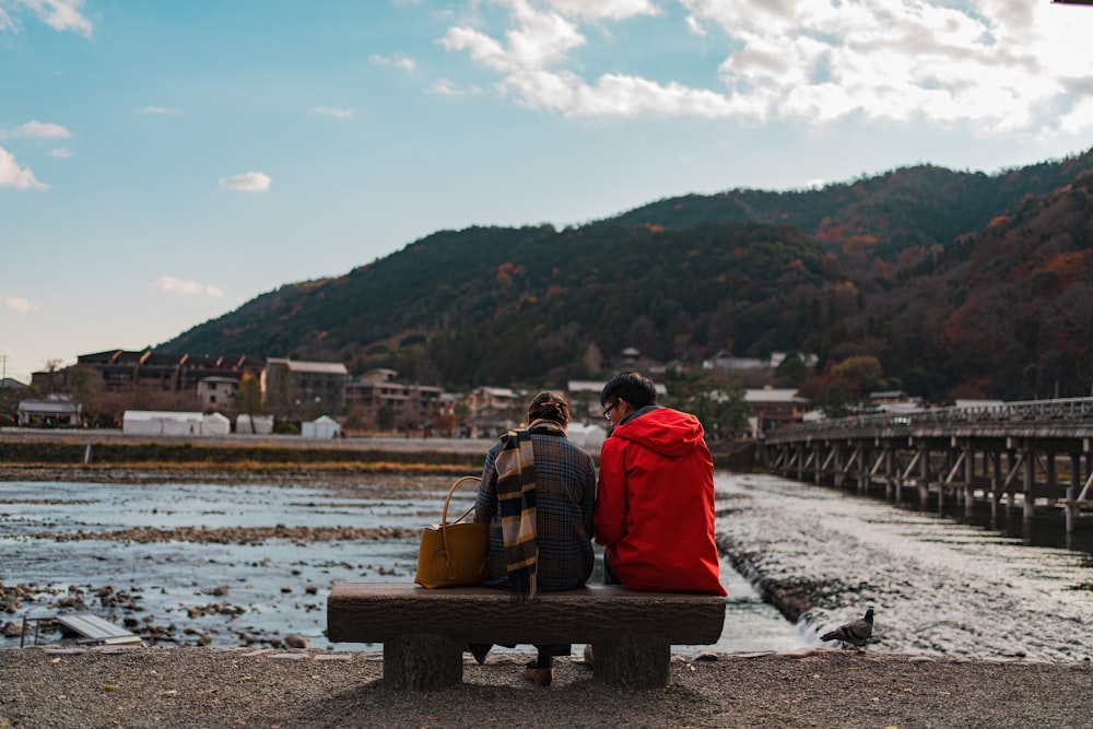 two person sitting on bench beside body of water