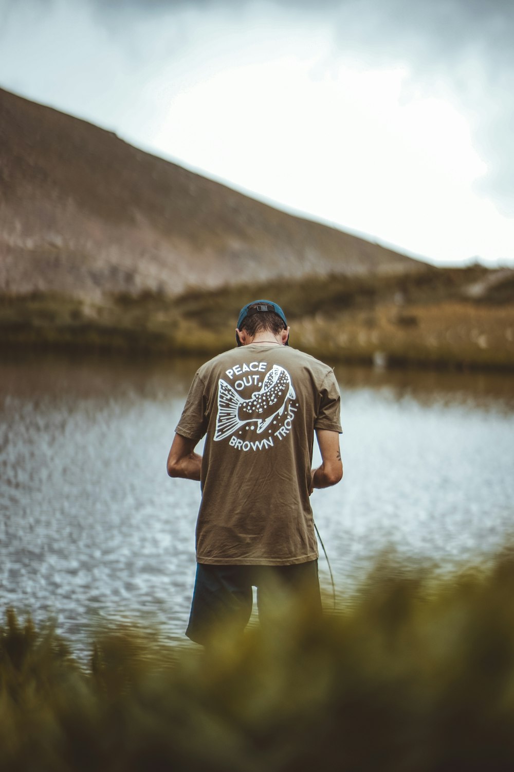 man in brown sweater standing beside body of water