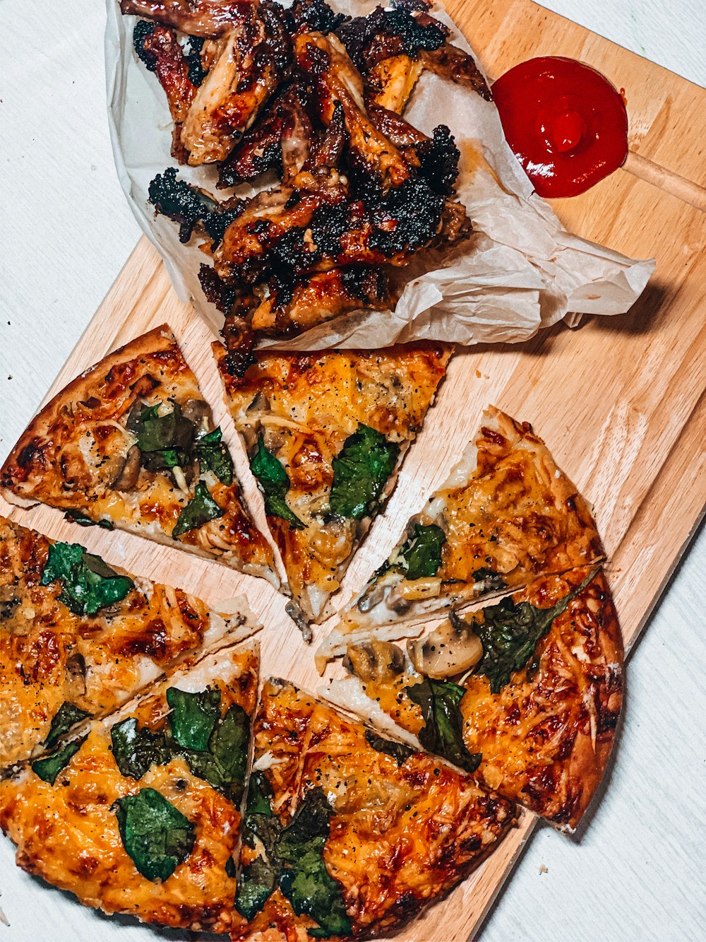 sliced pizza near grilled chicken with ketchup on a wooden chopping board