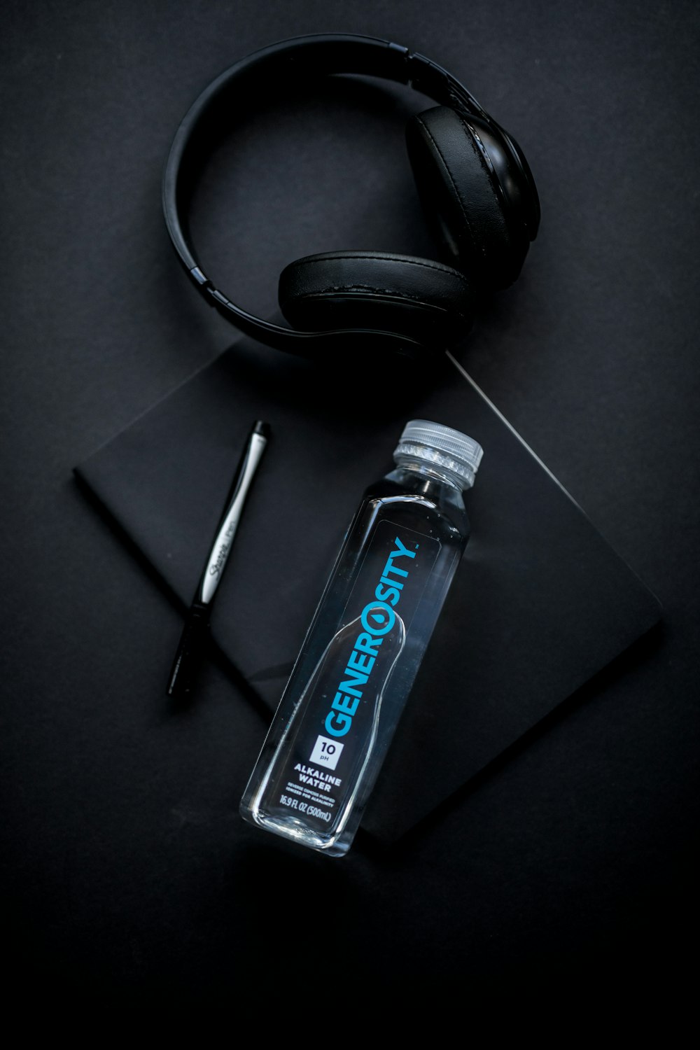 clear Generosity water bottle beside headphones and pen