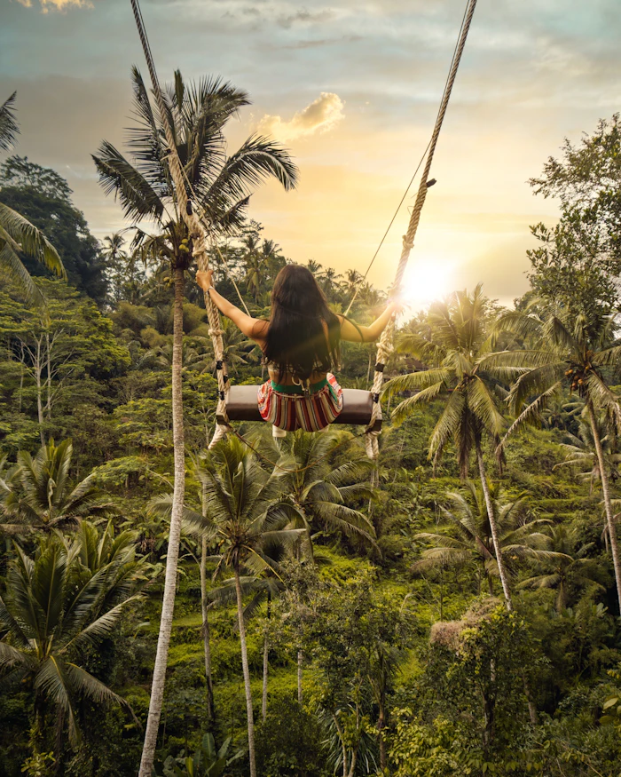 Wisatawan duduk di ayunan dengan latar hutan hijau