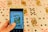 A hand is holding a smartphone displaying a close-up image of playing cards, specifically a King of Hearts and an Ace of Clubs. In the background, several playing cards are spread out, featuring various suits and numbers, slightly blurred for depth of field.