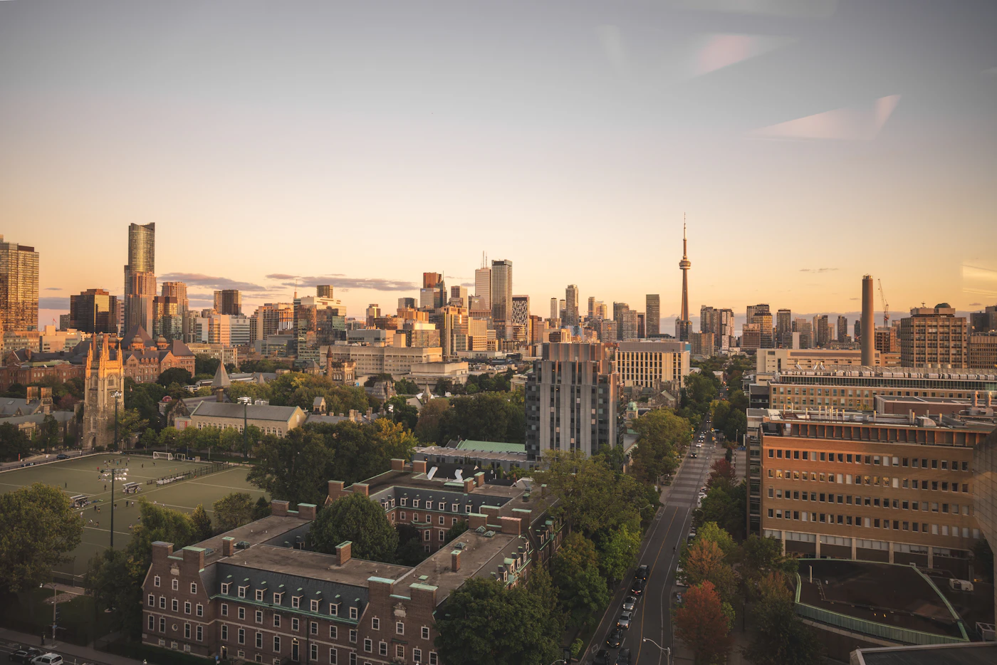 A wide golden-hour view of Toronto with the University campus quadrangle in the foreground and the downtown skyline beyond