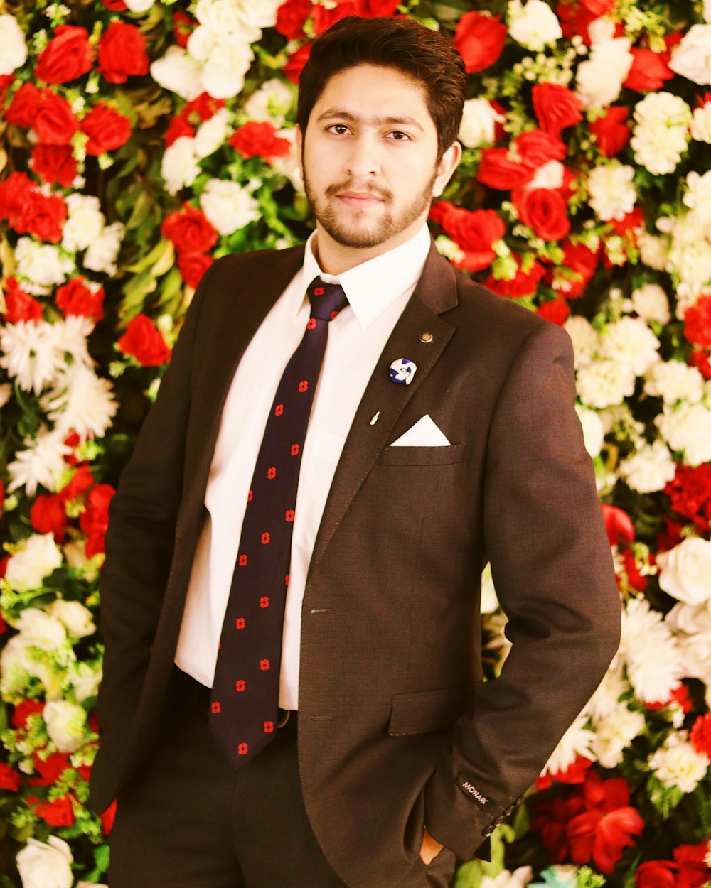 man in black suit standing in front of red and white flower bouquet