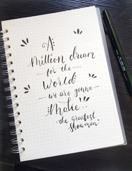 Close-up of hands writing goals on a notepad with a motivational quote in the background.