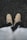 A pair of beige boots worn by a person standing on a rough, dark textured surface, possibly asphalt. The boots are laced up, and part of the person's clothing, including a sweater or jacket, is visible in the lower portion of the image.