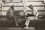 grayscale photo of two men sitting on bench