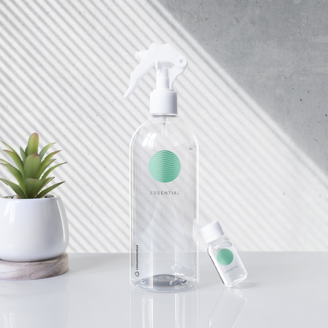 Clear glass spray bottle with a green label next to a small potted plant