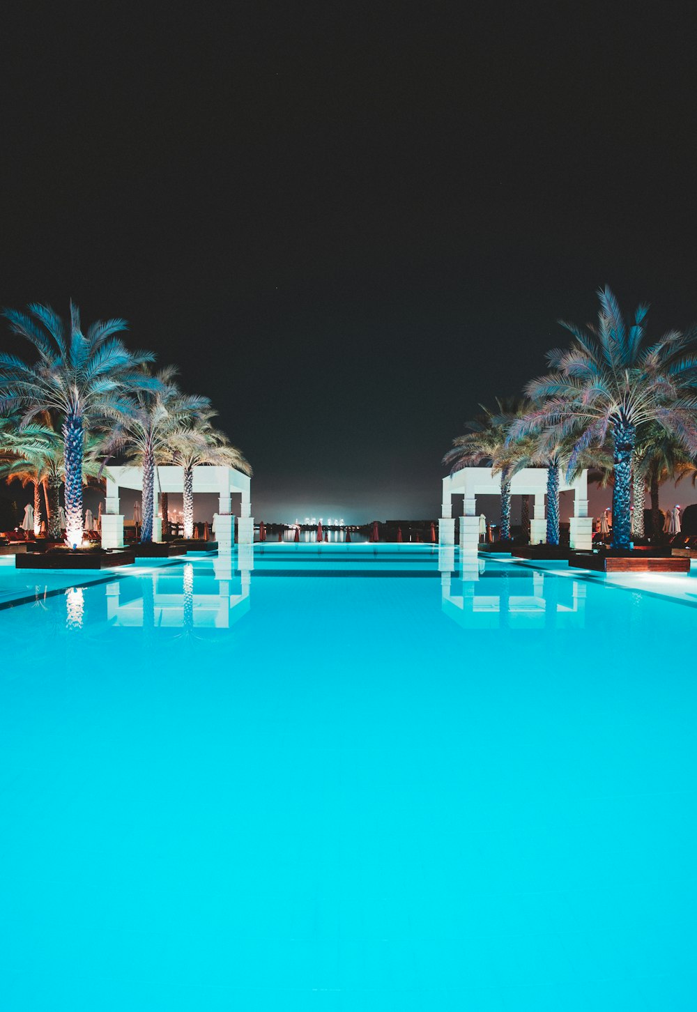Swimmingpool zwischen grünen Palmen bei Nacht